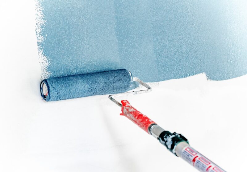 Muur verven strakke lijnen doe je eenvoudig in elke ruimte Blue paint being rolled onto an empty white wall with an extended paint roller