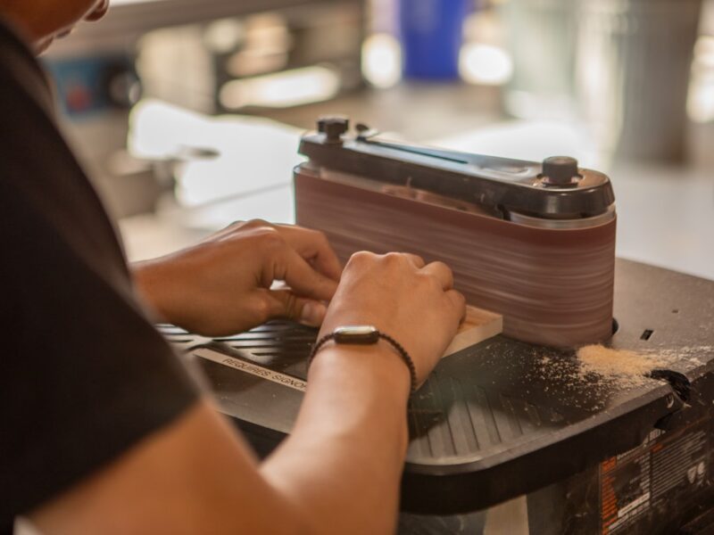 Handen schuren een houten plank op een bandschuurmachine